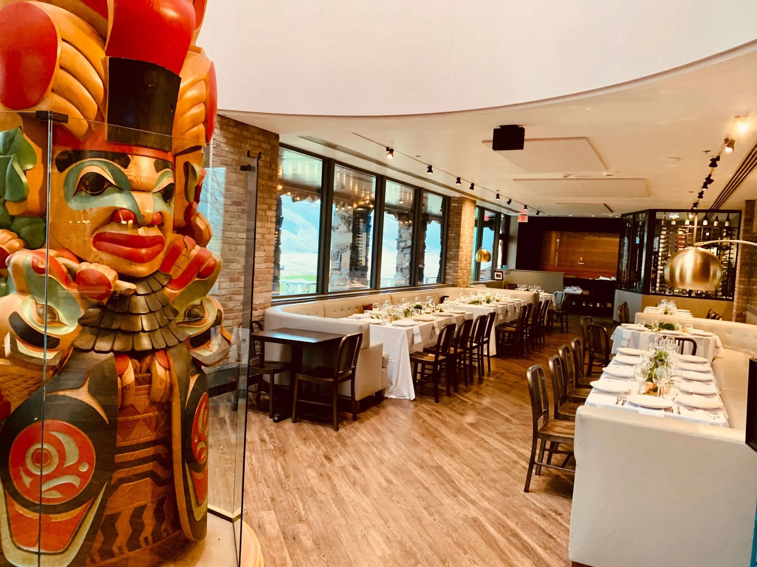 Interior of a dining establishment featuring a vibrant totem sculpture, elegant table settings, and large windows showcasing scenic views, highlighting the upscale dining experience in Jackson Hole.