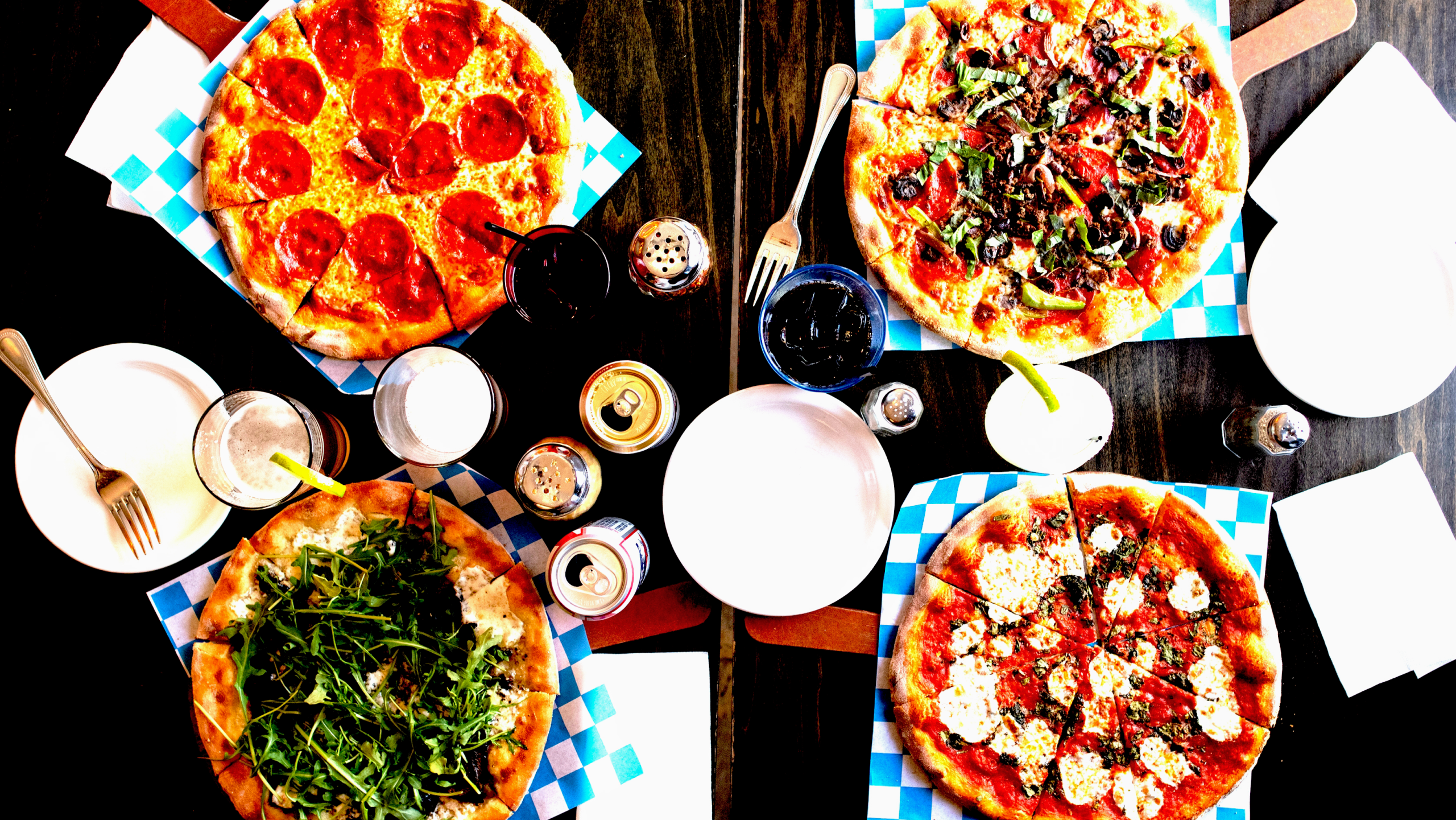 Wood-fired Neapolitan pizzas with various toppings, craft drinks, and dining utensils on a table, showcasing a casual dining experience in Jackson Hole.