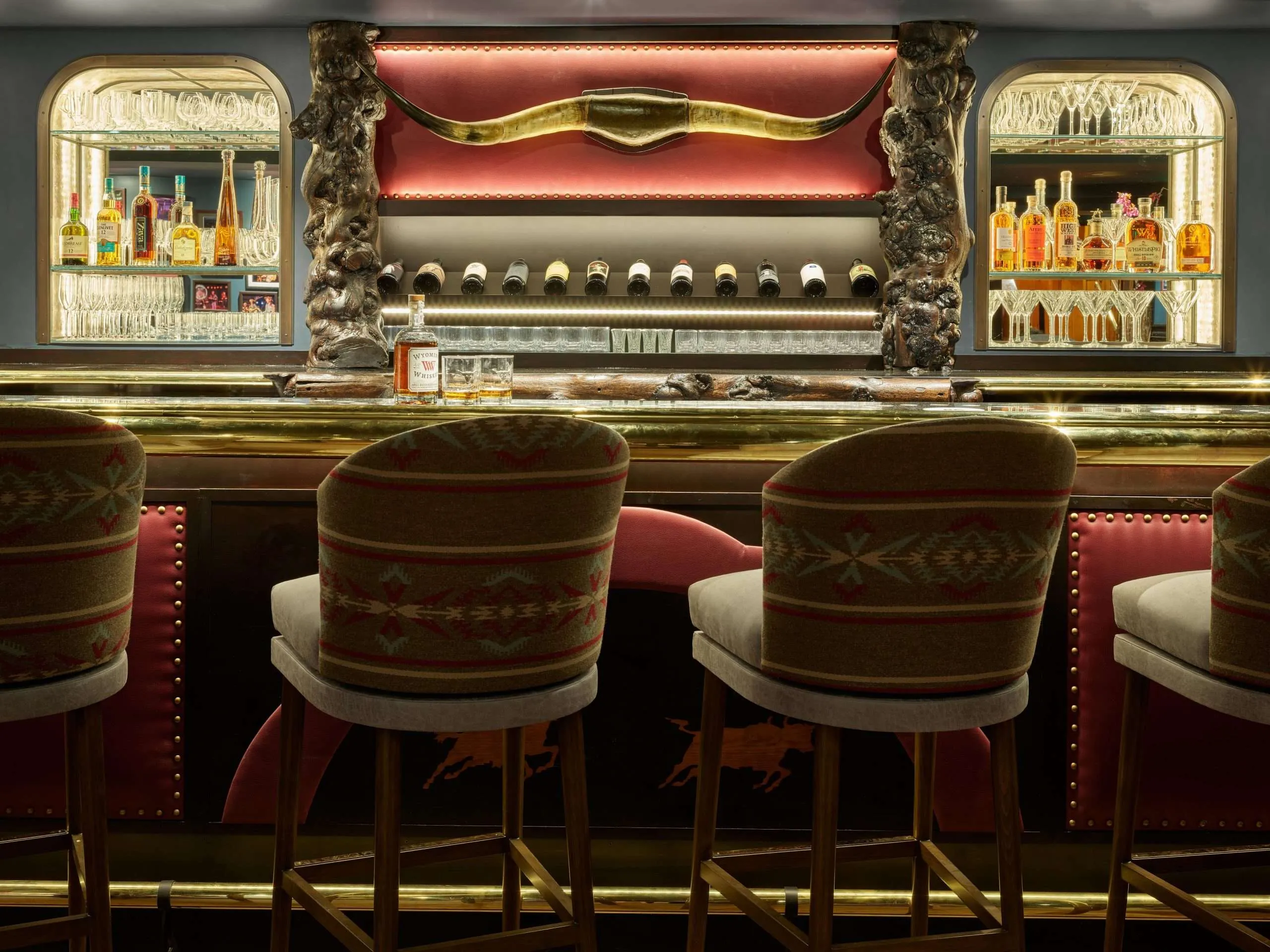 Elegant bar setting with decorative bullhorn, backlit shelves displaying premium spirits and wines, and stylish seating, reflecting the upscale dining atmosphere in Jackson Hole.