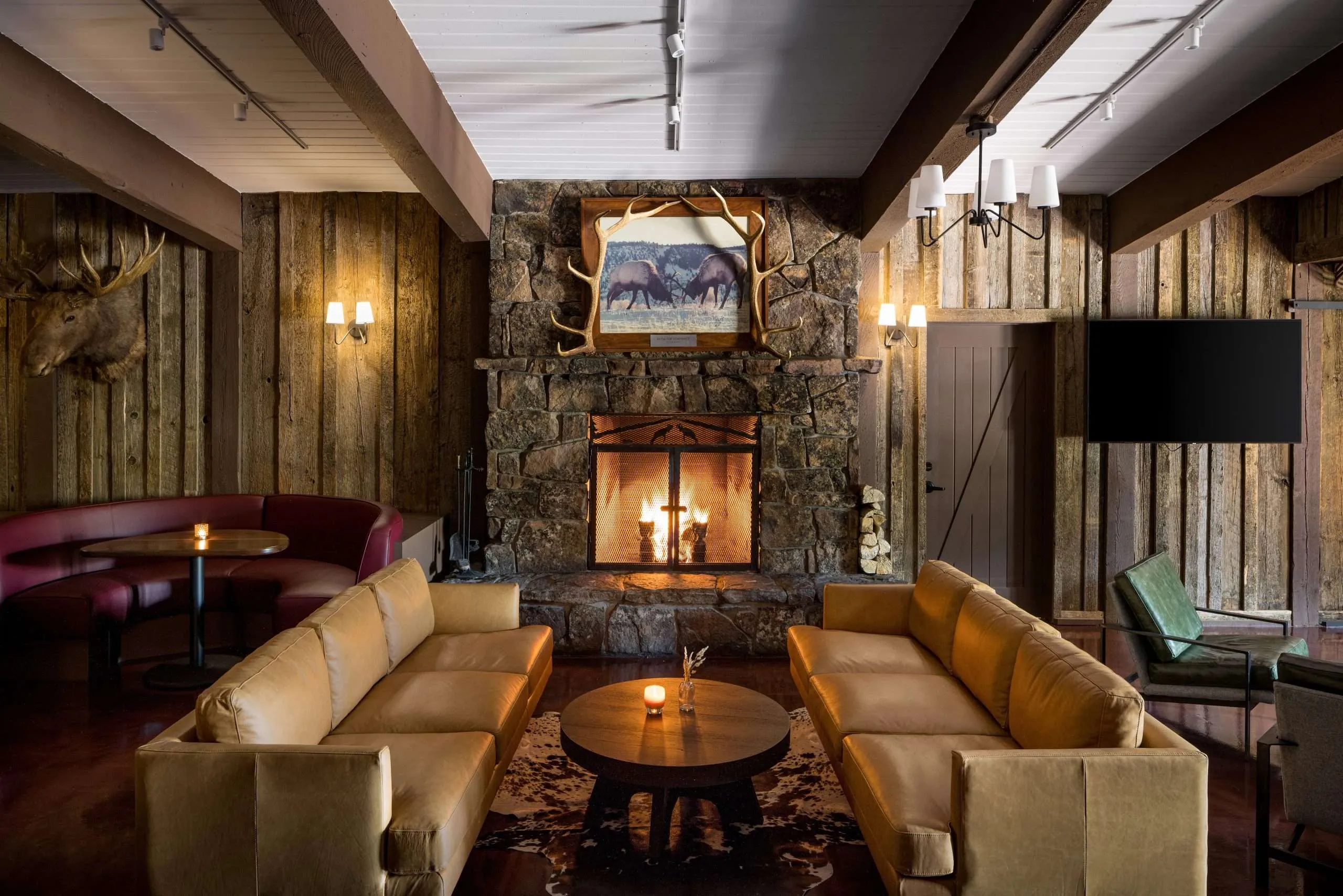 Cozy interior of a rustic lounge featuring leather sofas, a stone fireplace, and wooden accents, ideal for dining and relaxation in Jackson Hole.