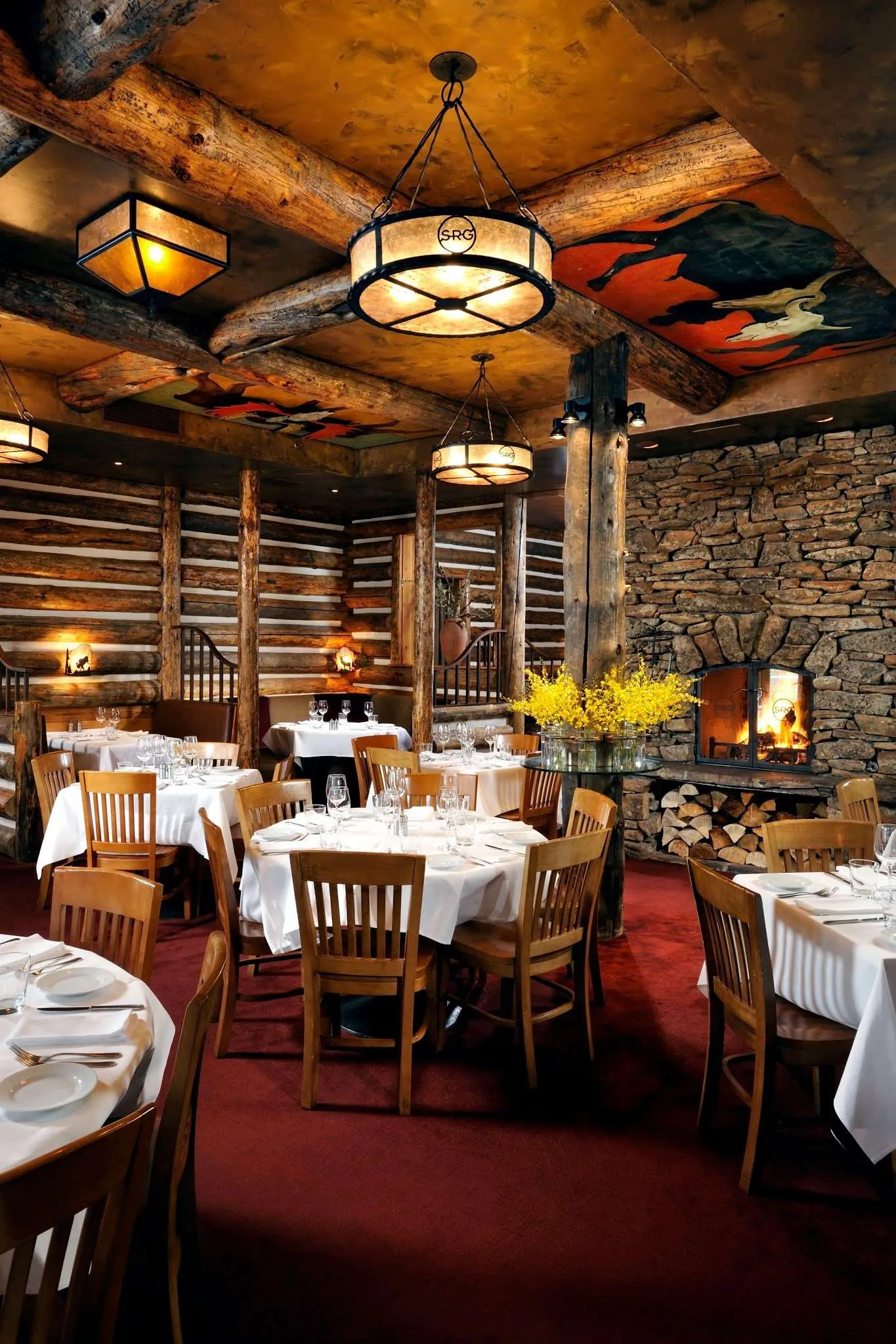 Elegant dining interior of a rustic restaurant featuring wooden beams, stone walls, and tables set with white linens, showcasing a warm atmosphere ideal for a fine dining experience in Jackson Hole.