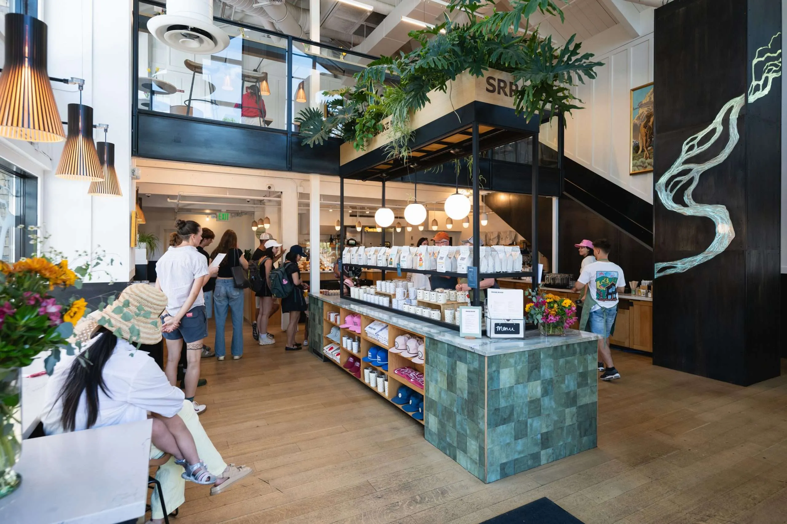 Coffee shop interior with customers in line, modern design, green plants, and a menu display at the counter, reflecting dining options in Jackson Hole.