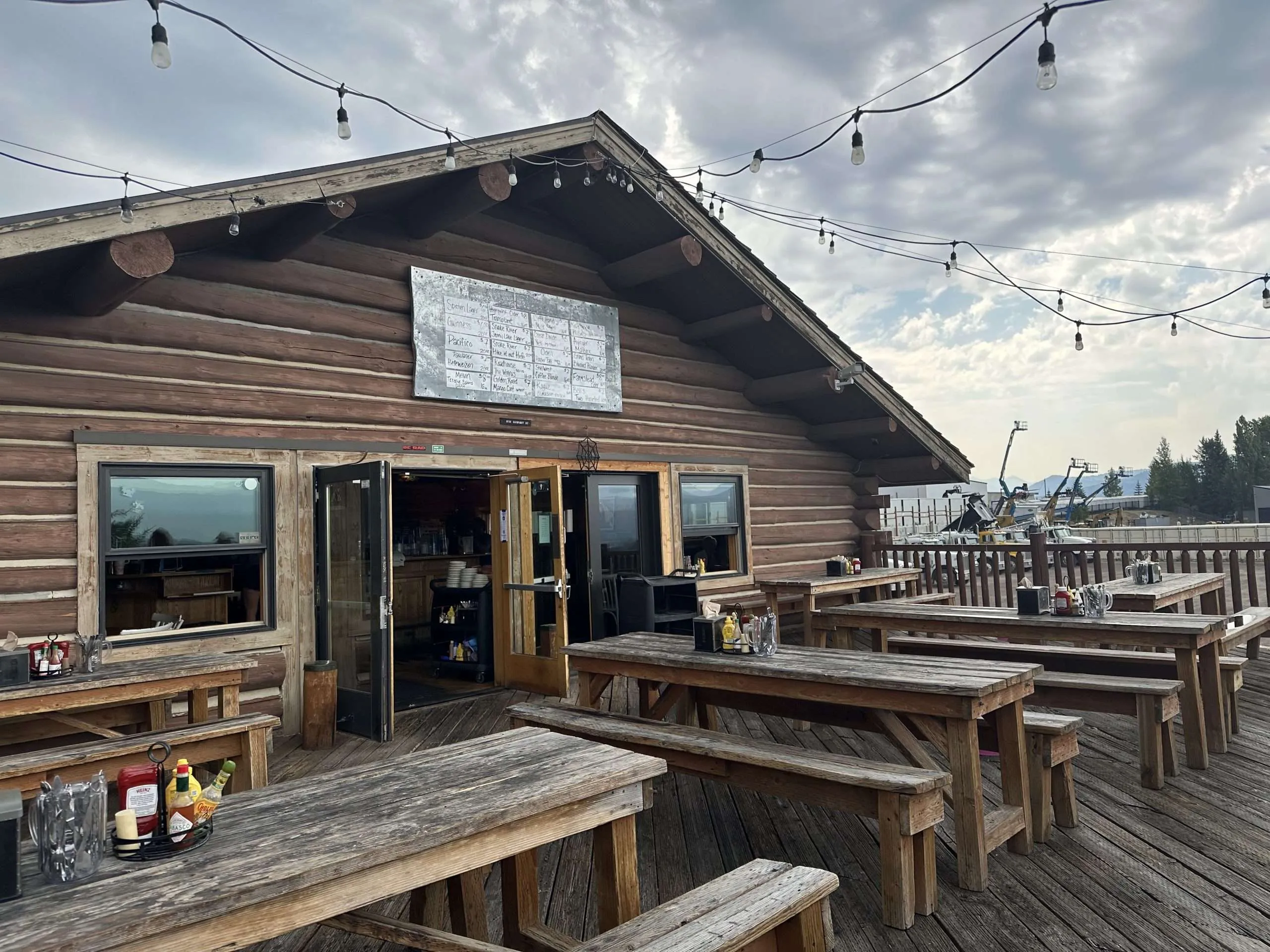 Outdoor dining area of a rustic restaurant with wooden tables, string lights, and a menu board, showcasing a welcoming atmosphere for visitors in Jackson Hole.