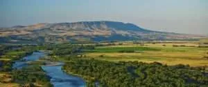Scenic view of a winding river surrounded by lush greenery and rolling hills in Jackson Hole, reflecting the natural beauty relevant to Steve Duerr's real estate offerings.