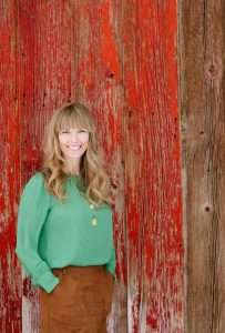 Mindy White, realtor with Jackson Hole Sotheby's International Realty, smiling in front of a rustic red wooden background, showcasing her approachable and professional demeanor.