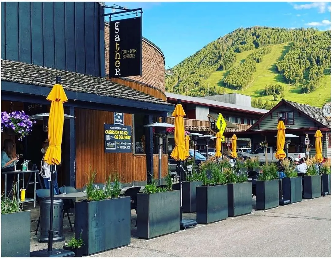Gather restaurant exterior with yellow umbrellas, outdoor seating, and mountain backdrop, showcasing modern American dining in Jackson Hole.