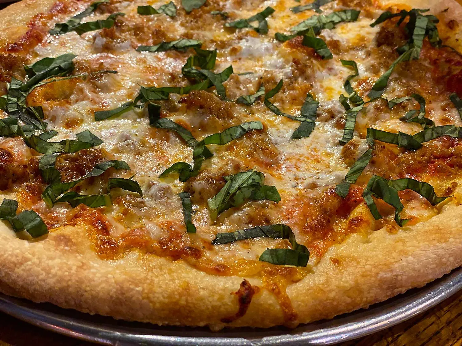 New York-style pizza topped with melted cheese, sausage, and fresh basil, served in a casual dining setting at Pinky Gs Pizzeria in Jackson Hole.