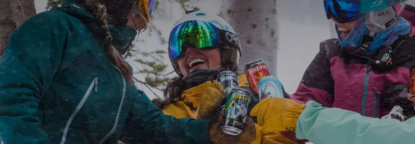 Friends enjoying craft beers outdoors in snowy setting, showcasing Melvin Brewing cans, highlighting local brewery culture in Jackson Hole.