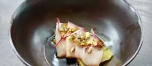 Delicate sushi dish featuring thin slices of fish topped with microgreens and pistachios, served in a modern bowl, representing The Kitchen's Asian-influenced fine dining menu.